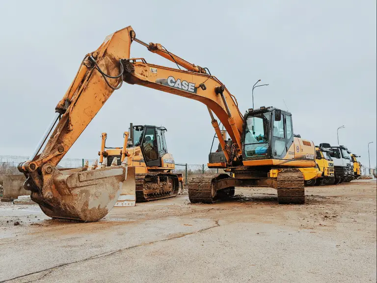 Tracked hydraulic excavator with its boom raised, parked on a contractor's yard beside a crawler dozer