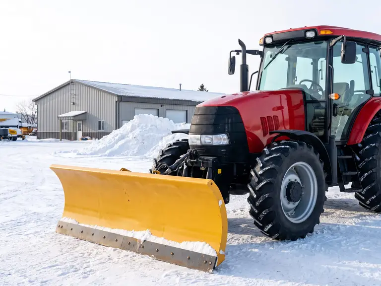 Utility tractor with an enclosed cab and a wide front snow plough blade