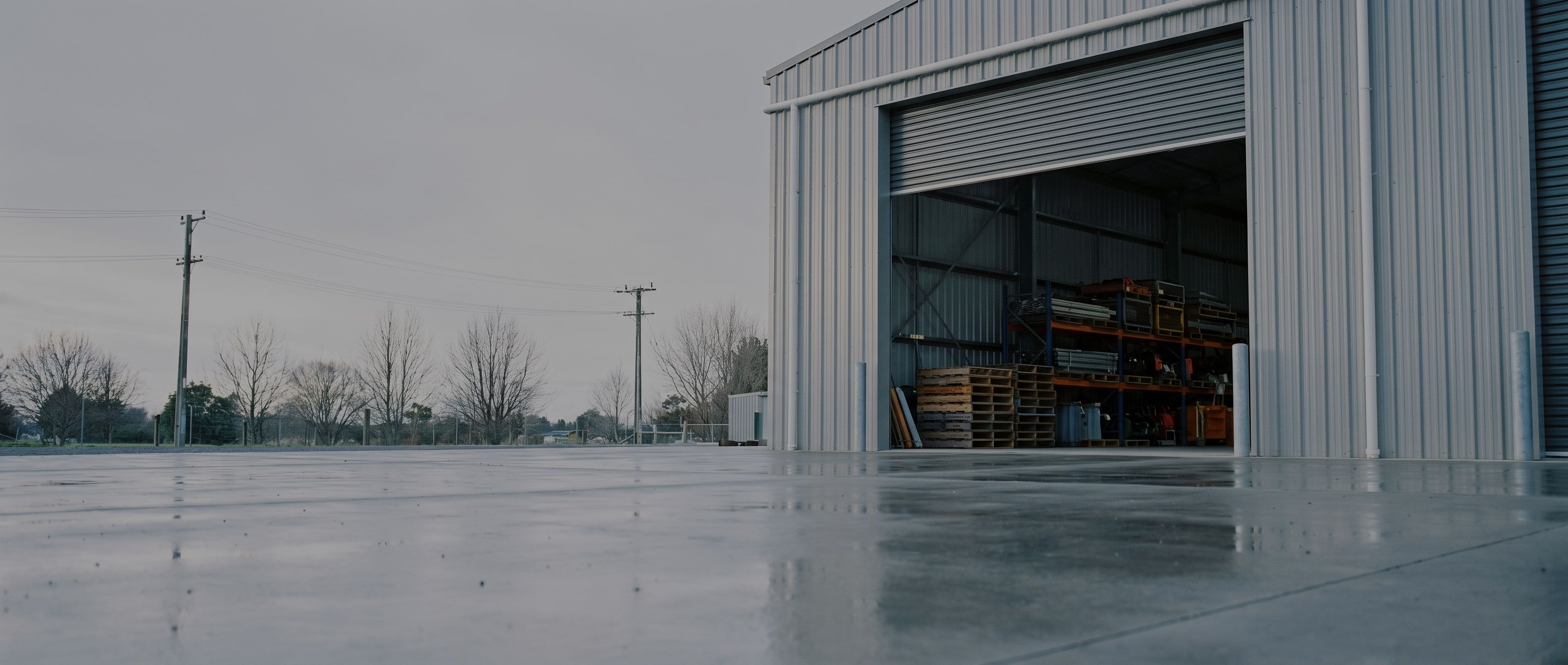A municipal works yard on a bright overcast morning, looking across wet concrete toward an open equipment bay