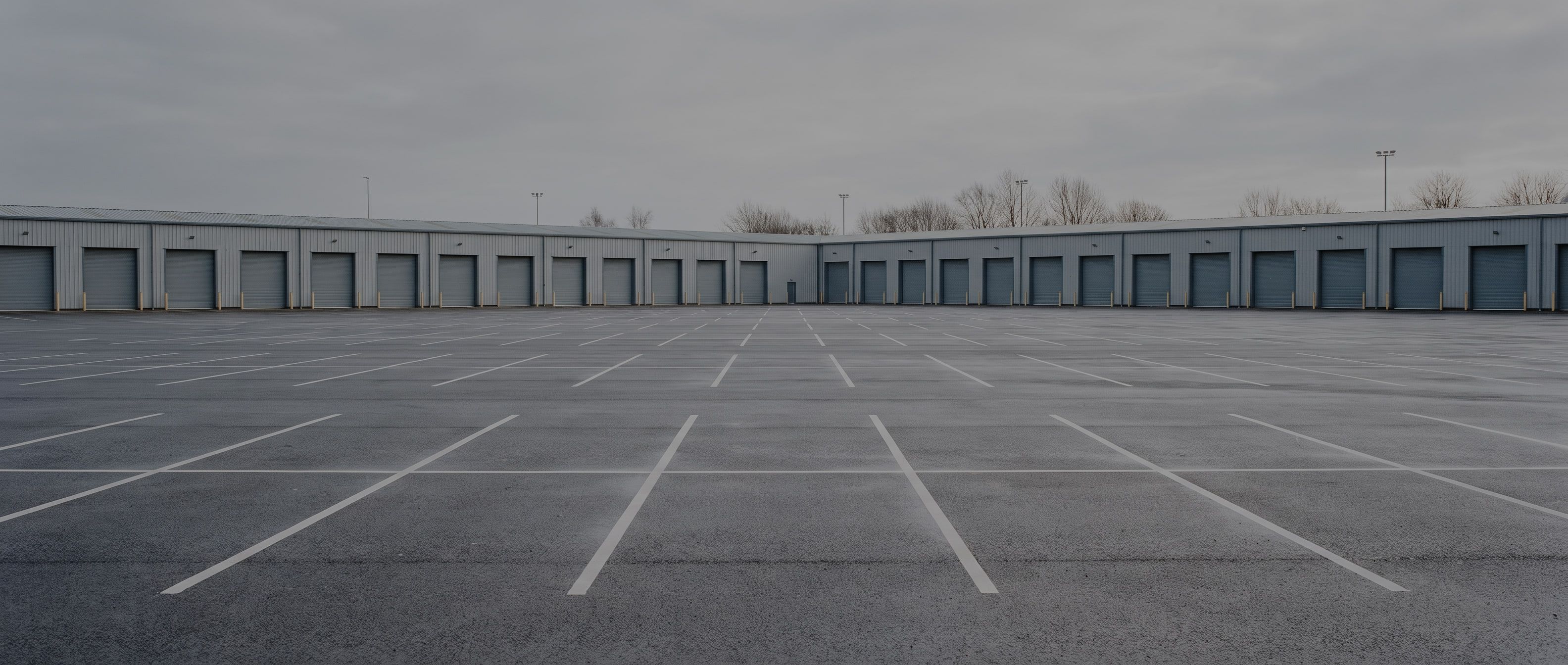 An empty commercial fleet parking apron at overcast dawn, painted bay lines on damp asphalt beside a low service building