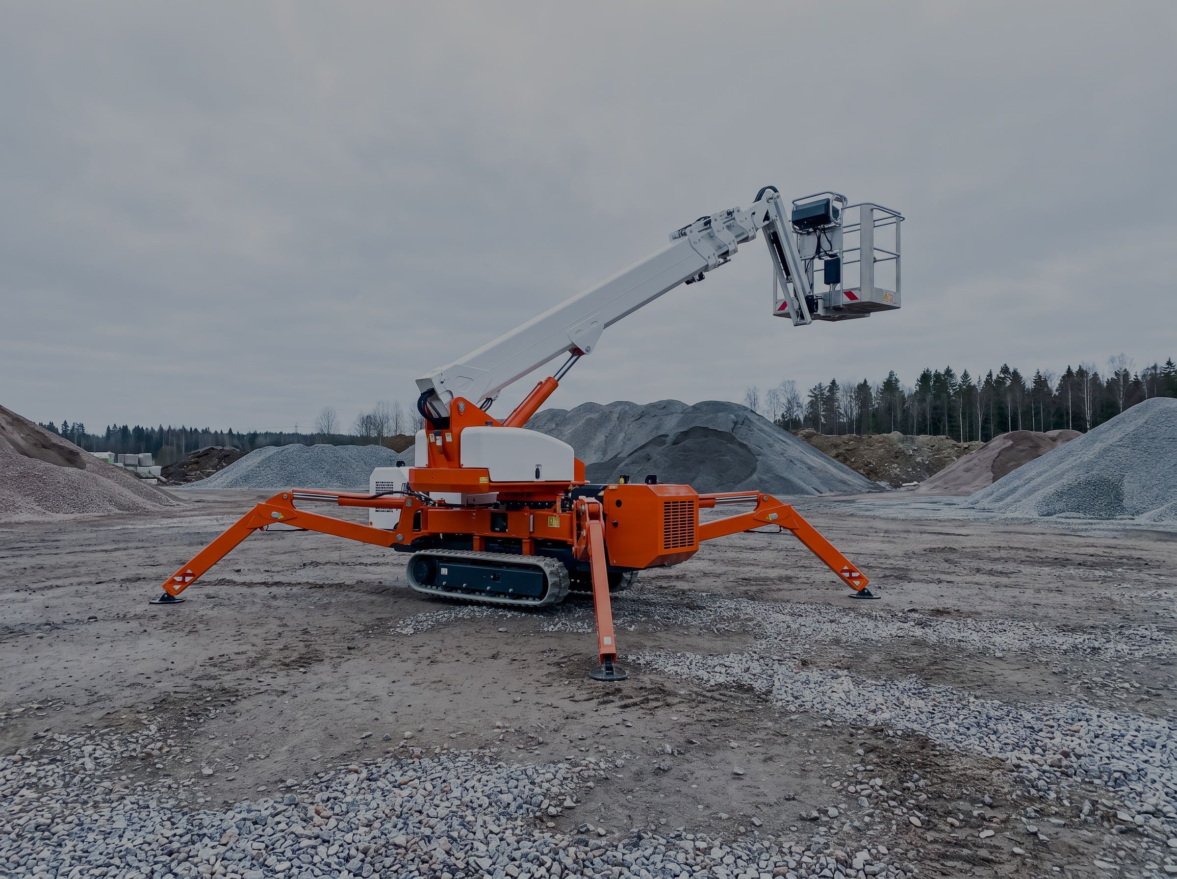 Tracked spider boom lift with its outriggers set down and platform raised in a gravel yard