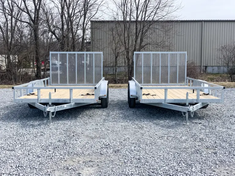 Flatbed utility equipment trailers with mesh ramp gates on a gravel yard